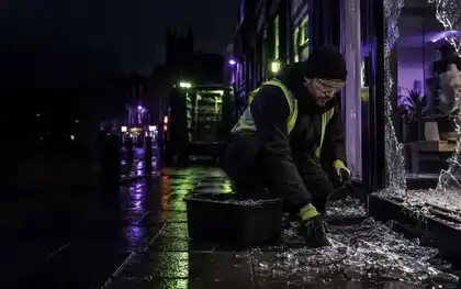 Glazier clearing shattered glass from a damaged window opening