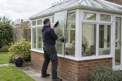 Glazier fitting a replacement side pane in a white-framed conservatory