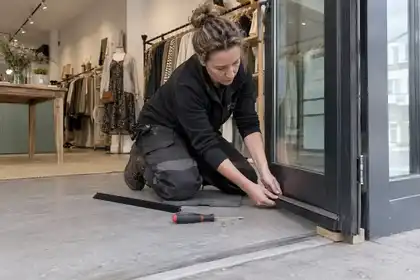 Tradesperson replacing a weather strip on a glazed shop door